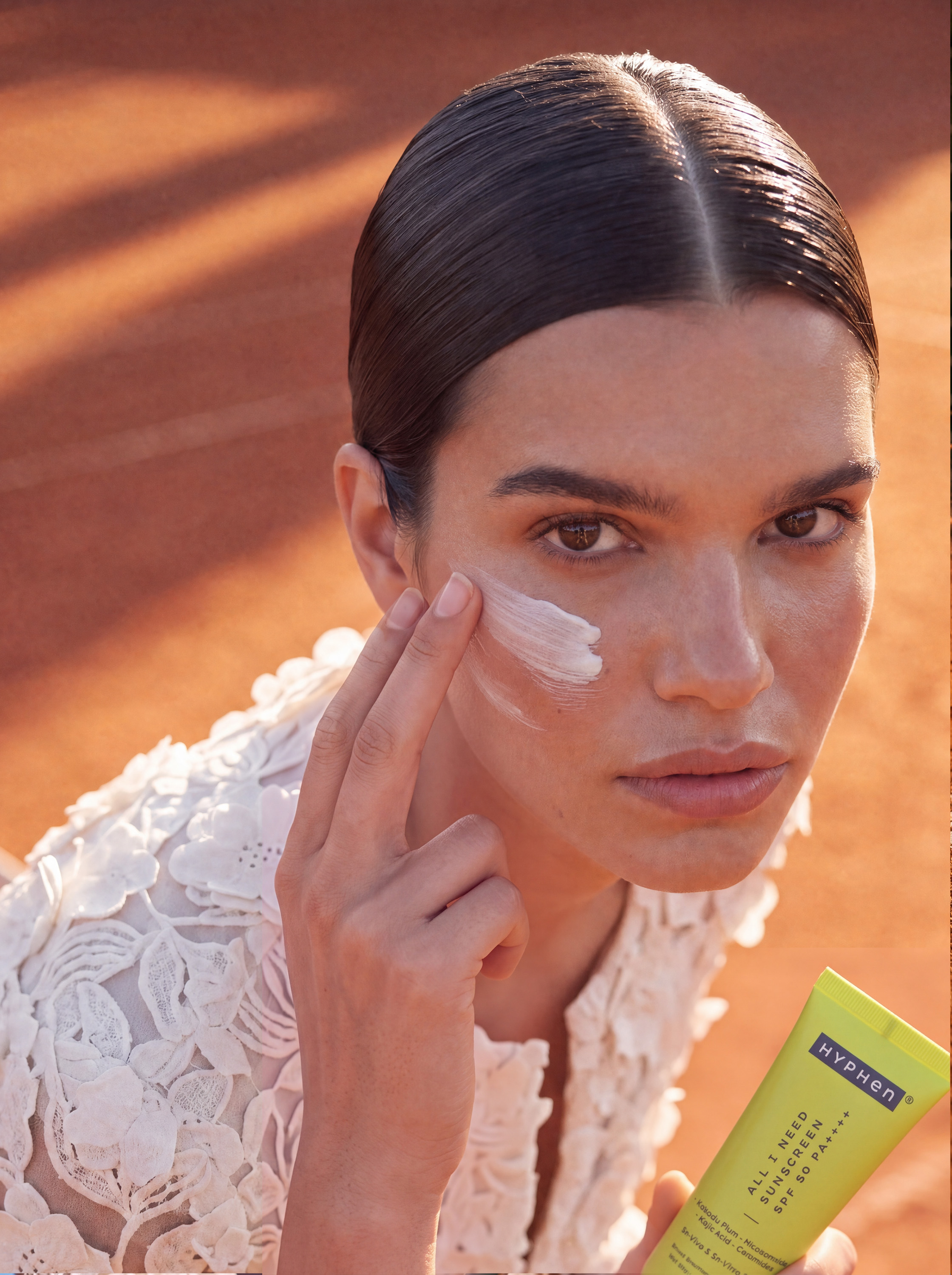 Close-up: model applying HYPHeN sunscreen to cheek, skin texture visible