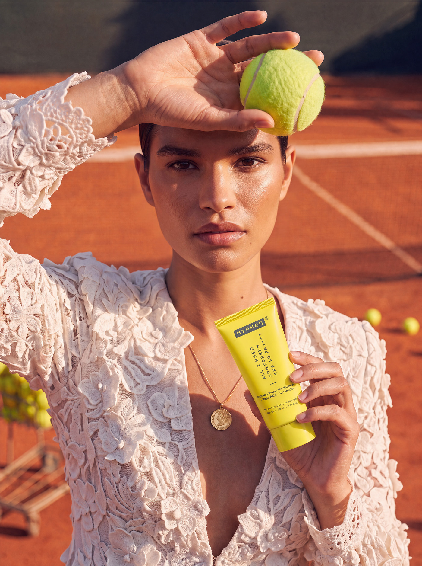 Model holding product and tennis ball raised to forehead, direct gaze